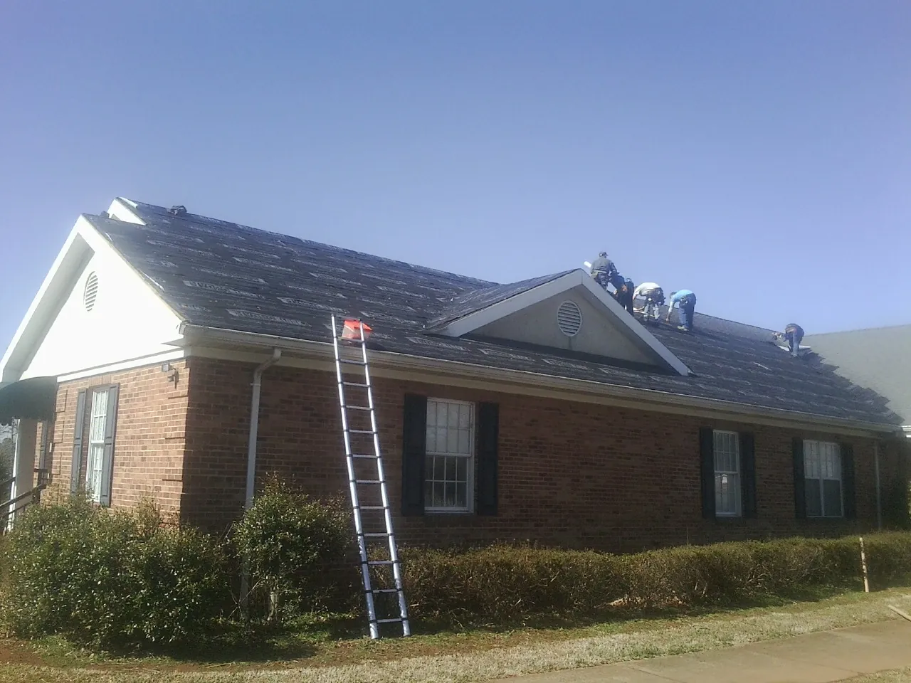 Crew tearing shingles off a brick ranch roof with a ladder set — Metal Roof Repair work by our crew in Fort Recovery