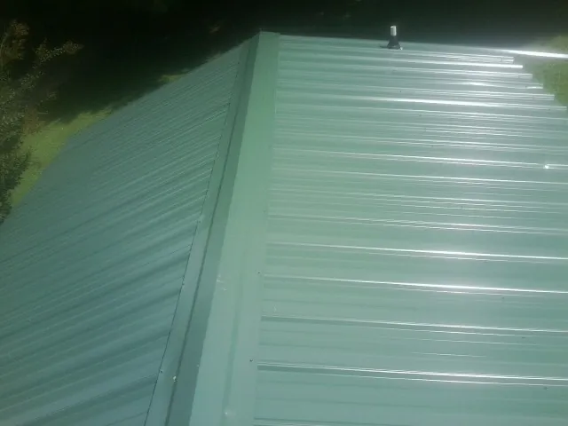 New green metal panels meeting at the ridge of a roof — Flat Roof Repair work by our crew in Fort Recovery