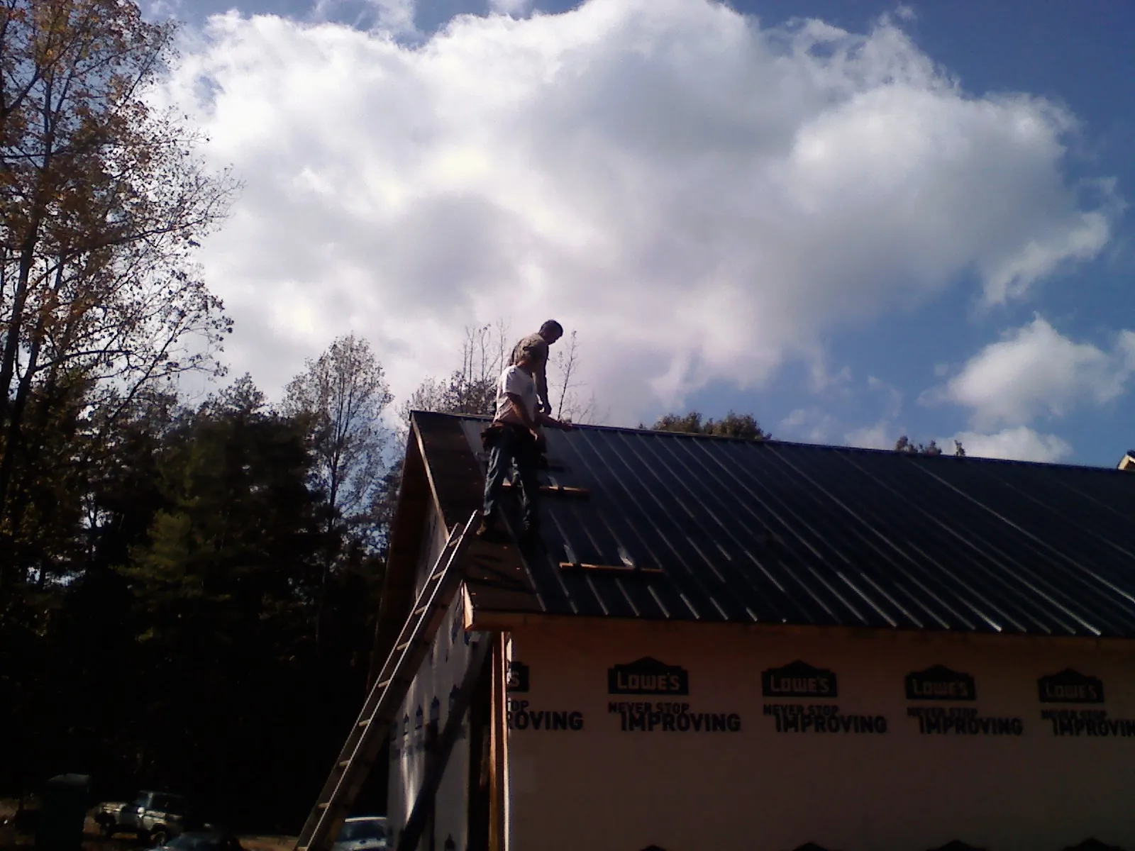 Roofer fastening dark metal panels high against a cloudy sky, from a Roof Inspection job in Fort Recovery