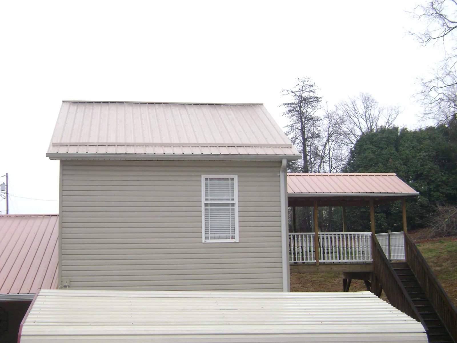 Tan metal roofs on a two story addition and attached porch, from a Roof Replacement job in Fort Recovery